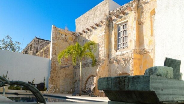 Un edificio histórico con fachada de piedra, una palmera y un área de piscina.