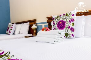 A hotel room with two beds, white bedding, floral pillows, and a neatly folded white towel. - Socaire Hotel (Campeche)