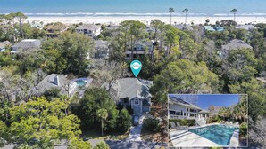 An aerial view of a residential area with houses surrounded by trees, a beach, and a swimming pool.