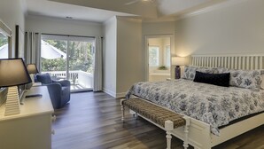 A bedroom with a bed, a ceiling fan, a nightstand, a lamp, a bench, and a view of the outdoors through a sliding glass door.