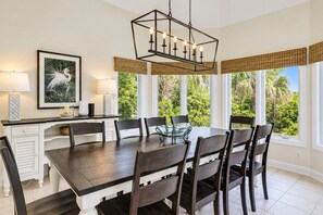 A dining area with a dark wooden table, six chairs, a glass-top center table, and a pendant light fixture.