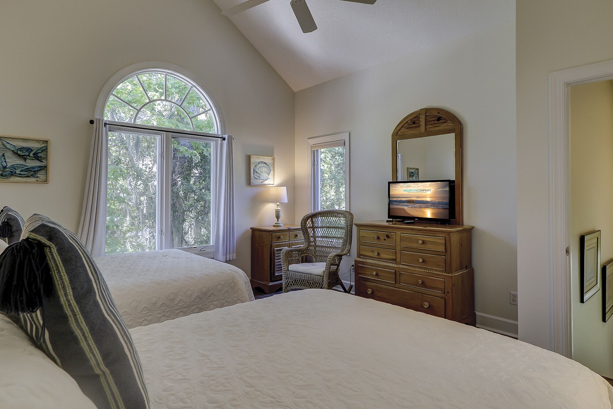 A bedroom with two beds, a dresser, a chair, a television, and a large window with a view of trees.