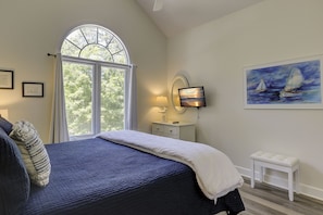 A bedroom with a large bed, a nightstand, a TV, a painting, and a window with curtains.
