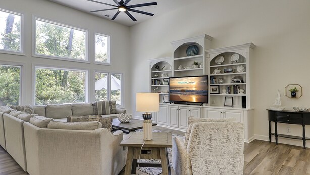 A spacious living room with a large TV, comfortable seating, and a view of the outdoors through large windows.