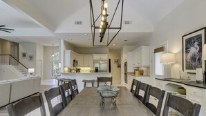A spacious dining area with a long table and chairs, a kitchen area with modern appliances, and a staircase leading to another level.