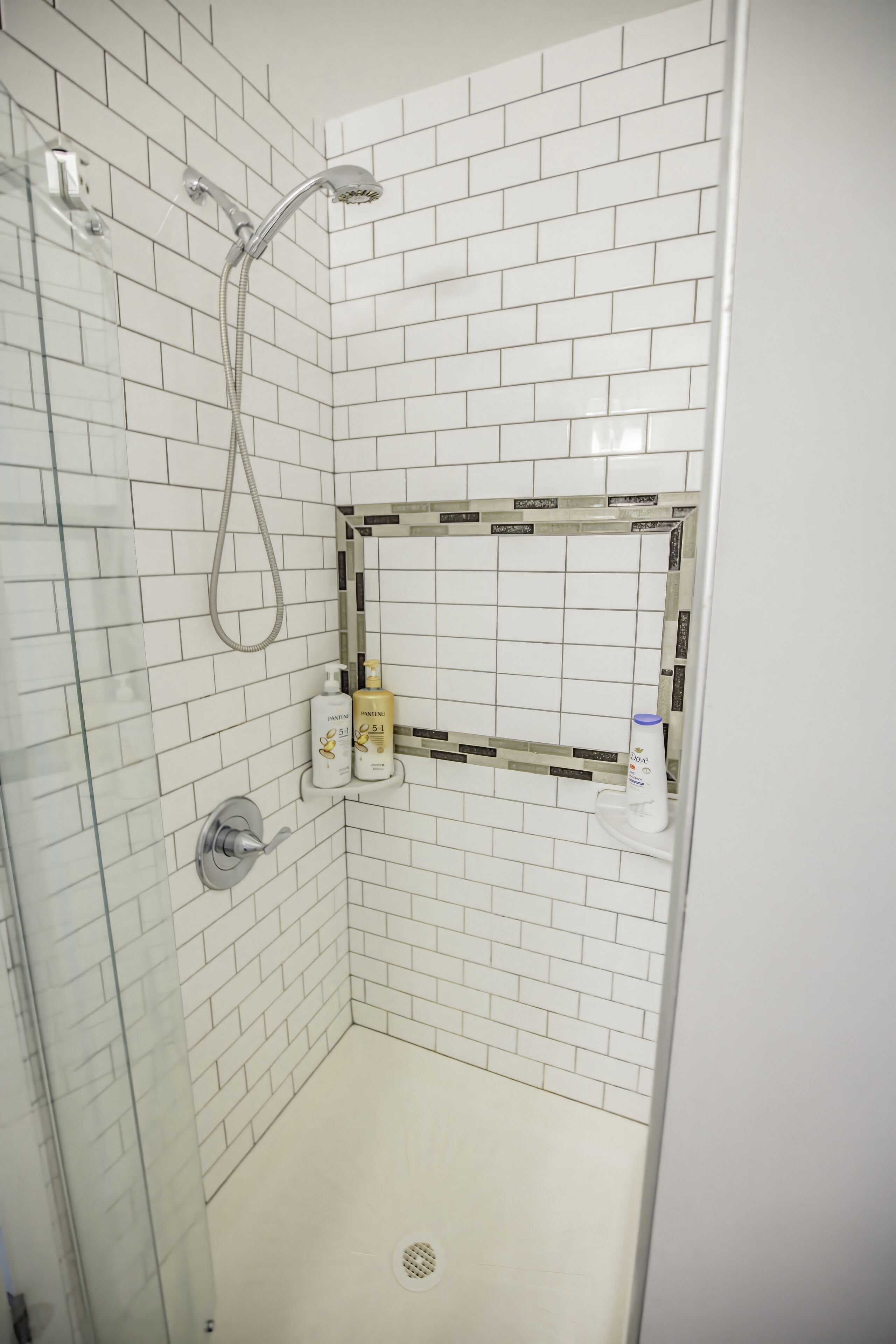 Ducha a pie con azulejos blancos tipo metro, puerta de cristal y ducha.