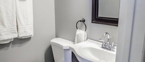 A bathroom with a white toilet, a sink with a mirror above it, and two towels hanging on hooks.