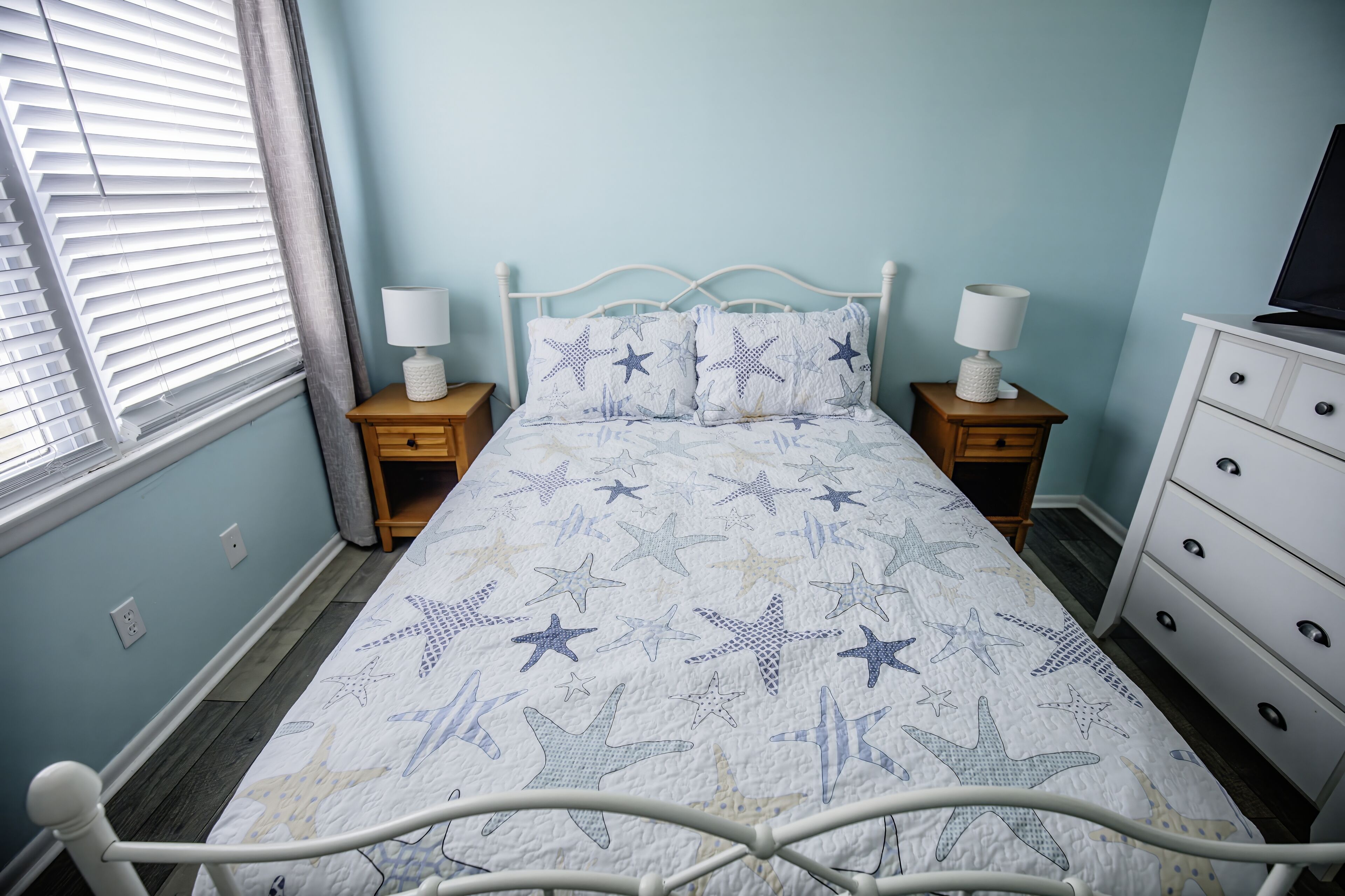 Een slaapkamer met een bed, twee nachtkastjes, een kaptafel en een raam met zonwering.