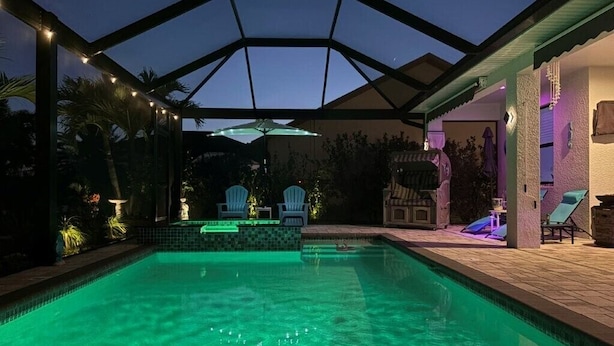 A swimming pool with a glass ceiling, surrounded by lounge chairs and a small waterfall feature. - South-facing Waterfront Villa 3BR w/ Heated Pool & Spa (Cape Coral)