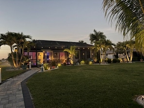 A modern building with a well-maintained lawn, outdoor seating area, and palm trees.