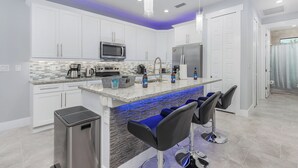 A modern kitchen with white cabinets, a central island with bar stools, a microwave, refrigerator, and a coffee maker. - South-facing Waterfront Villa 3BR w/ Heated Pool & Spa (Cape Coral)
