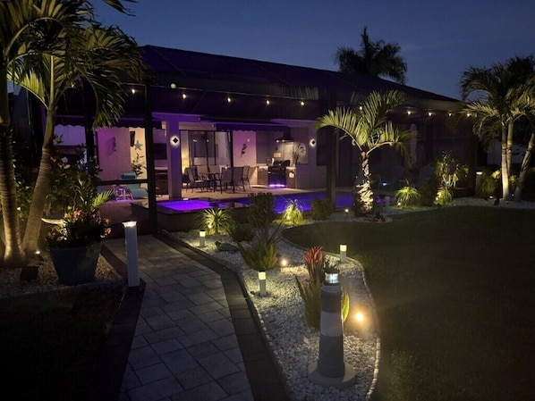 A modern house with a pool, outdoor seating, and well-lit pathways.