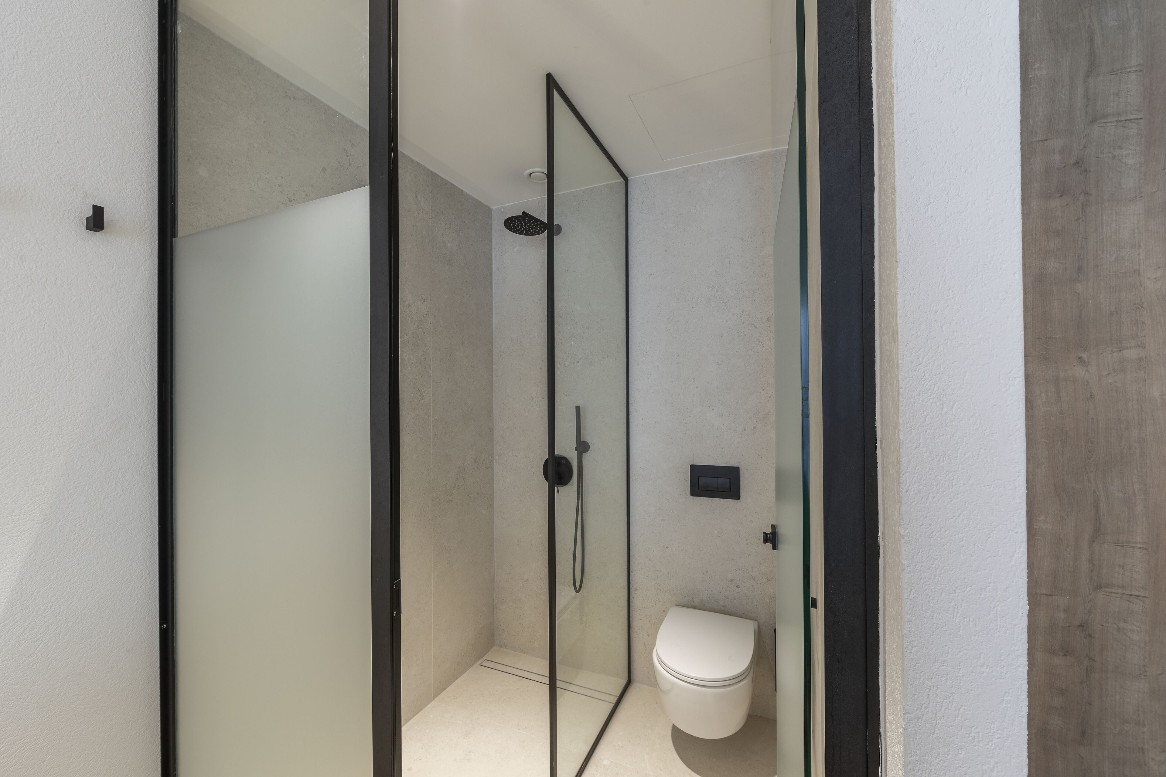 A modern bathroom with a glass-enclosed shower, a white toilet, and a minimalist design.