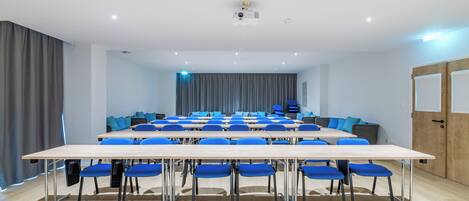 A conference room with a long table, blue chairs, and a projector on the ceiling.