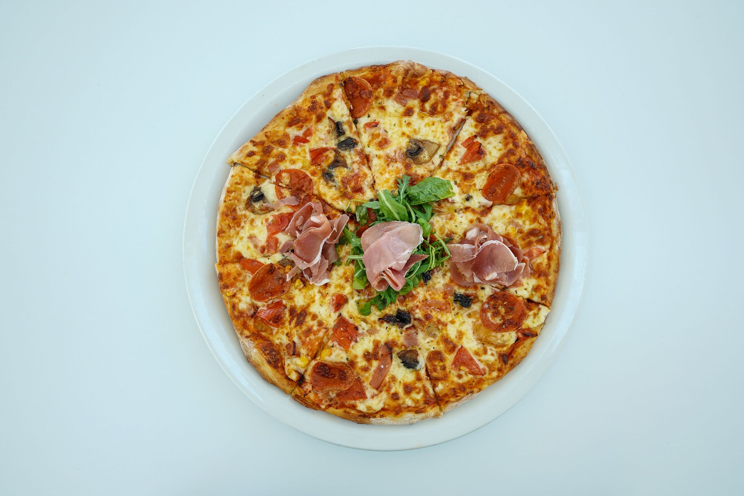 Pizza amb pepperoni, bolets i prosciutto damunt d'un plat blanc.