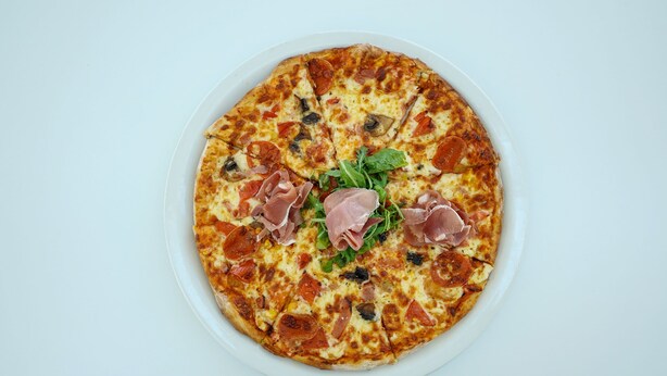 Una pizza con pepperoni, champiñones y prosciutto sobre un plato blanco.