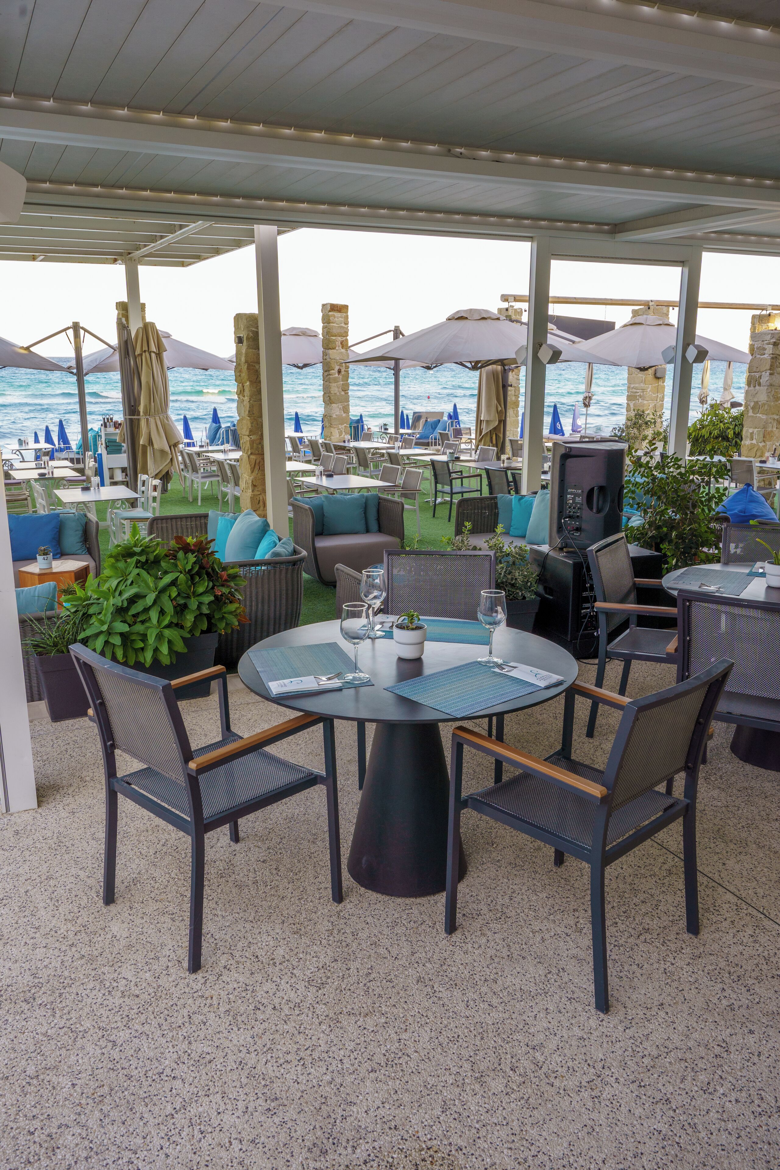 An outdoor seating area with tables and chairs, umbrellas, and a view of the sea.