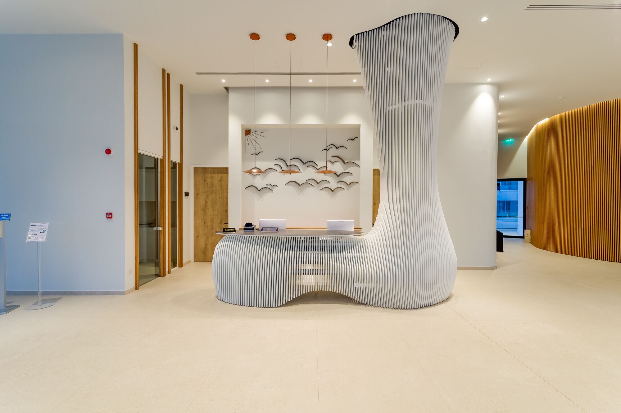 Un área de recepción moderna con un mostrador de diseño único con textura, una lámpara fijada a la pared y una puerta de madera.