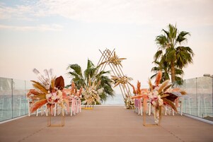 An outdoor wedding setup with floral arrangements and palm trees.