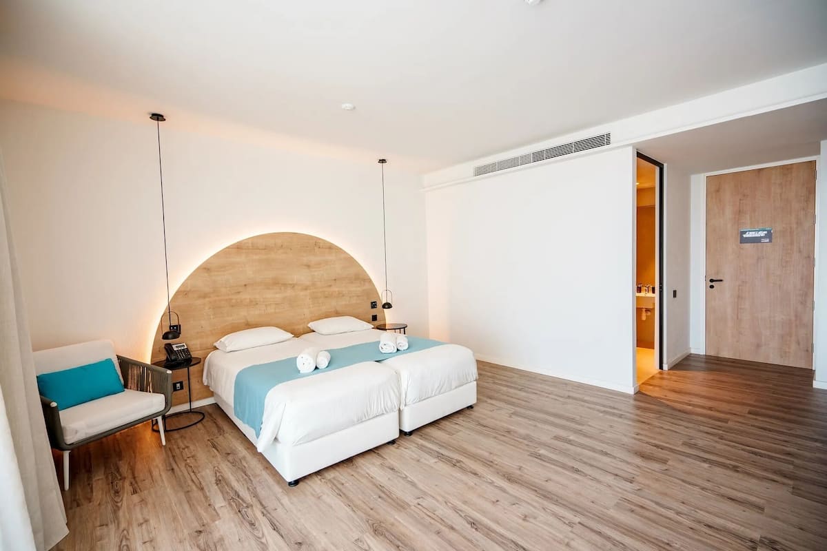 A modern hotel room with a large bed, a bedside table, a chair, and a wooden floor.