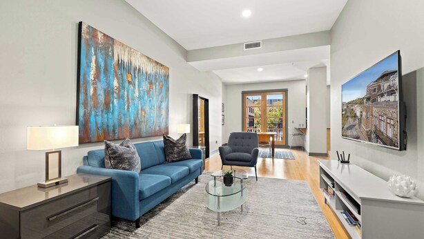 Een moderne woonkamer met een blauwe bank, een glazen salontafel en een groot abstract schilderij.