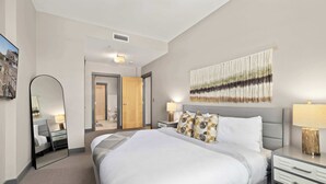 Een hotelkamer met een groot bed, nachtkastjes, een spiegel, wandtapijt en een deur naar een badkamer.