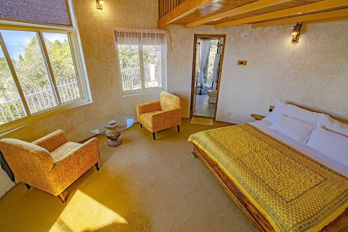 A bedroom with a bed, two chairs, a small table, and a window.