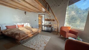 Une chambre à coucher avec un lit, une chaise, une petite table, une fenêtre et un escalier.