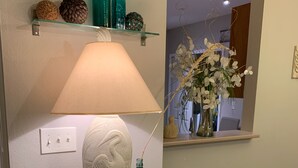 Um armário branco com portas de vidro, uma luminária, objetos decorativos e um vaso com flores.