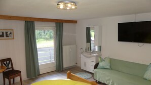 A bedroom with a bed, a sofa, a TV, a window with curtains, and a radiator.