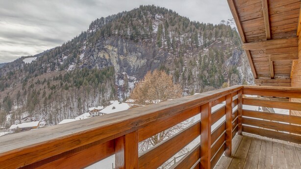 A wooden balcony with a view of a mountainous landscape.