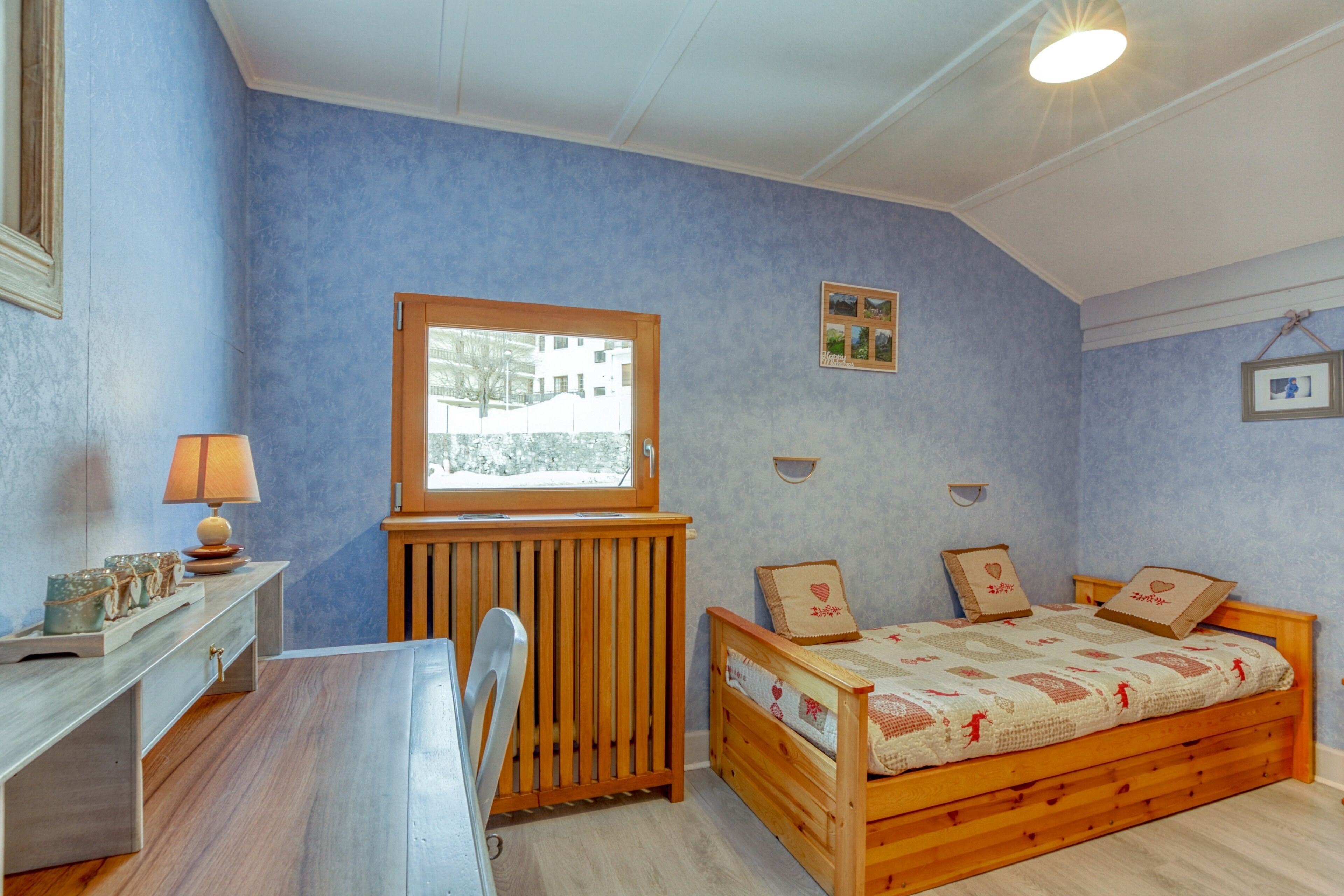 Ein Schlafzimmer mit einem Holzbett, einem Schreibtisch mit Lampe und einem Fenster mit Blick auf Gebäude.