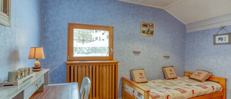 Ein Schlafzimmer mit einem Holzbett, einem Schreibtisch mit Lampe und einem Fenster mit Blick auf Gebäude.