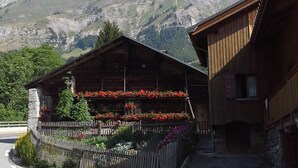A wooden building with a balcony adorned with flowers, set against a mountainous backdrop.