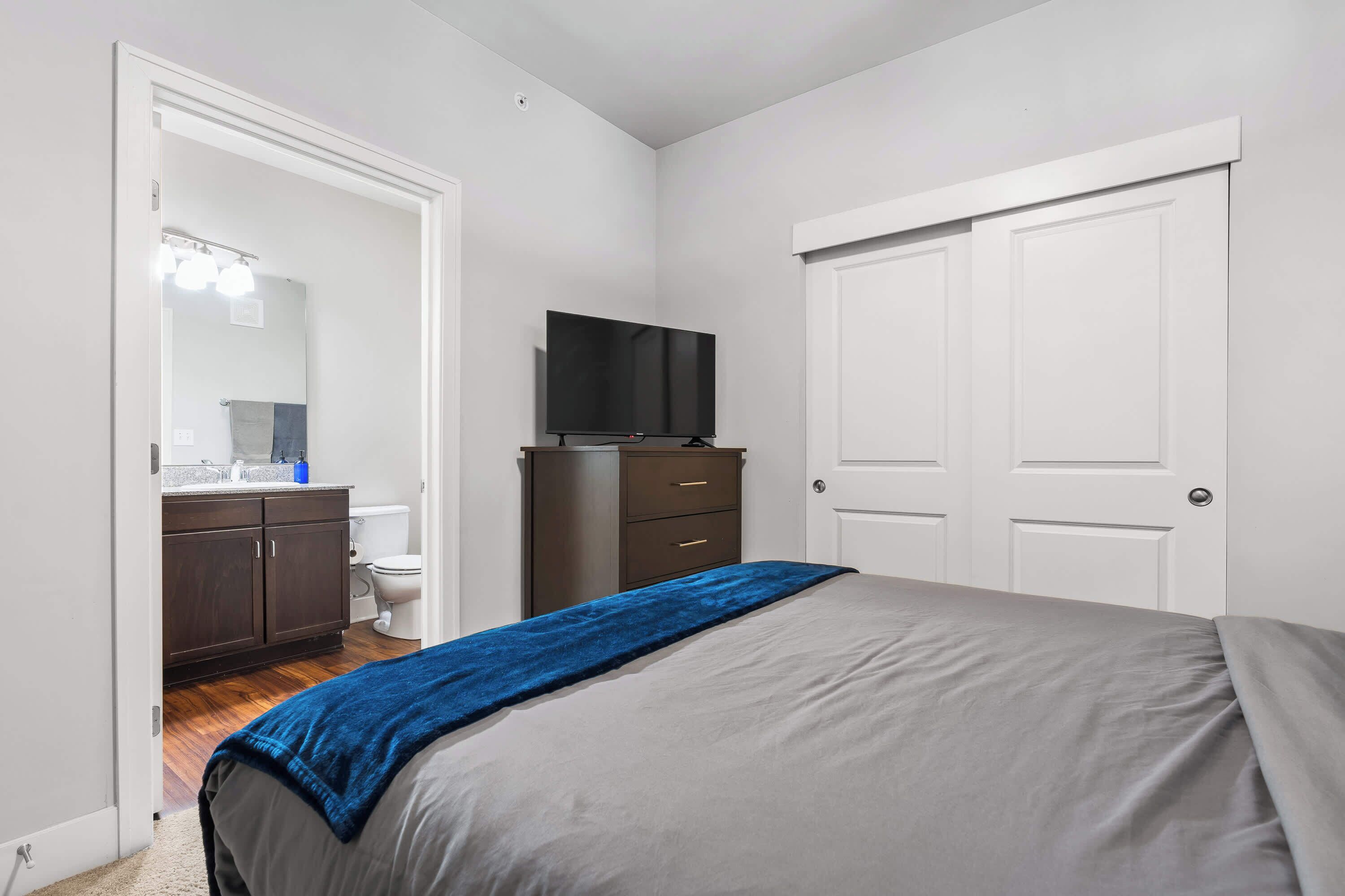 A bedroom with a bed, a television, a wardrobe, and a bathroom visible through an open door.