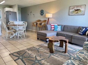 A living room with a grey sofa, white chairs, a wooden coffee table, and a patterned rug. - Sea Sounds | ★Beachfront★ | 2 Pools | First Floor Island Retreat 2 Bedroom Condo (Port Aransas)