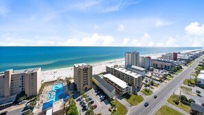 Un hôtel situé sur la côte, doté d’une piscine, offrant une vue sur la plage et comprenant plusieurs bâtiments.