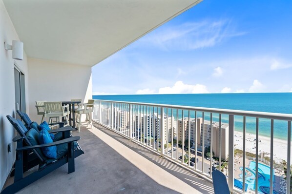 Un balcon avec vue sur l’océan et la plage, une piscine et un espace salon extérieur.