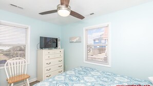 Un dormitorio con cama, cómoda, silla, ventilador de techo y ventanas.
