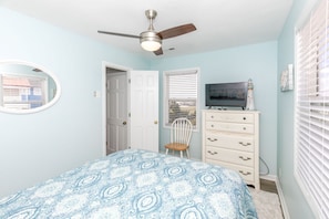 Un dormitorio con cama, ventilador de techo, cómoda, silla y televisor.