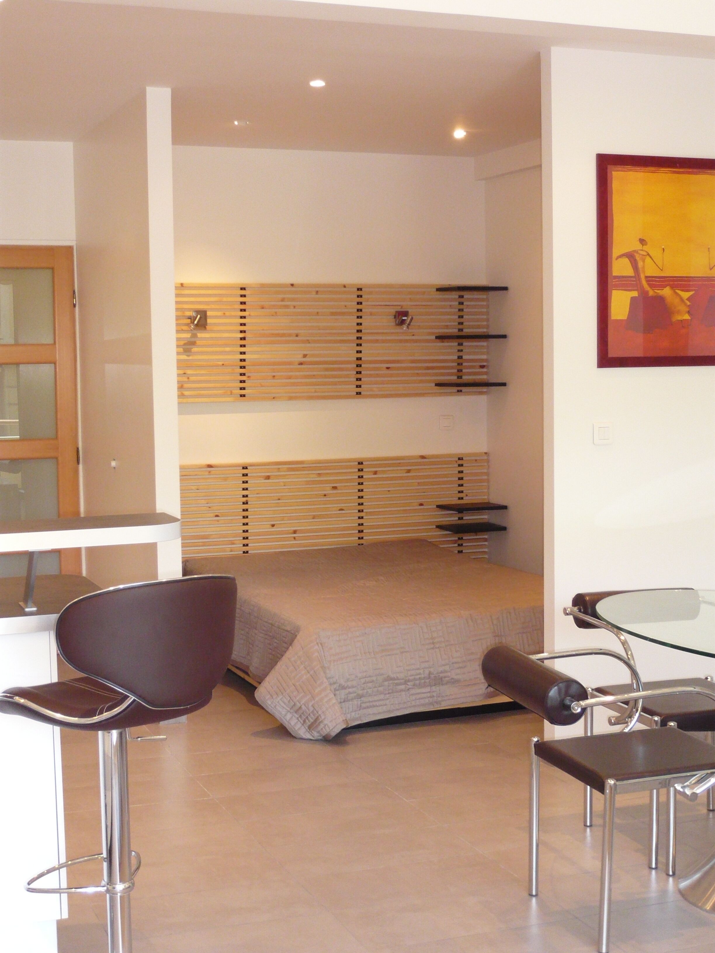 A modern hotel room with a bed, a desk, a chair, and a glass table.