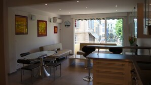 A modern kitchen with a dining area, featuring a large window with a city view, a built-in oven, and a seating area with a bench and chairs. - 2 /3 ROOMS NEAR BEACH AND CONVENTION CENTER 4 PEOPLE MAXIMUM (Alpes-Maritimes)