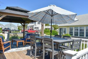 An outdoor deck with a table and chairs, a striped umbrella, and a covered seating area.