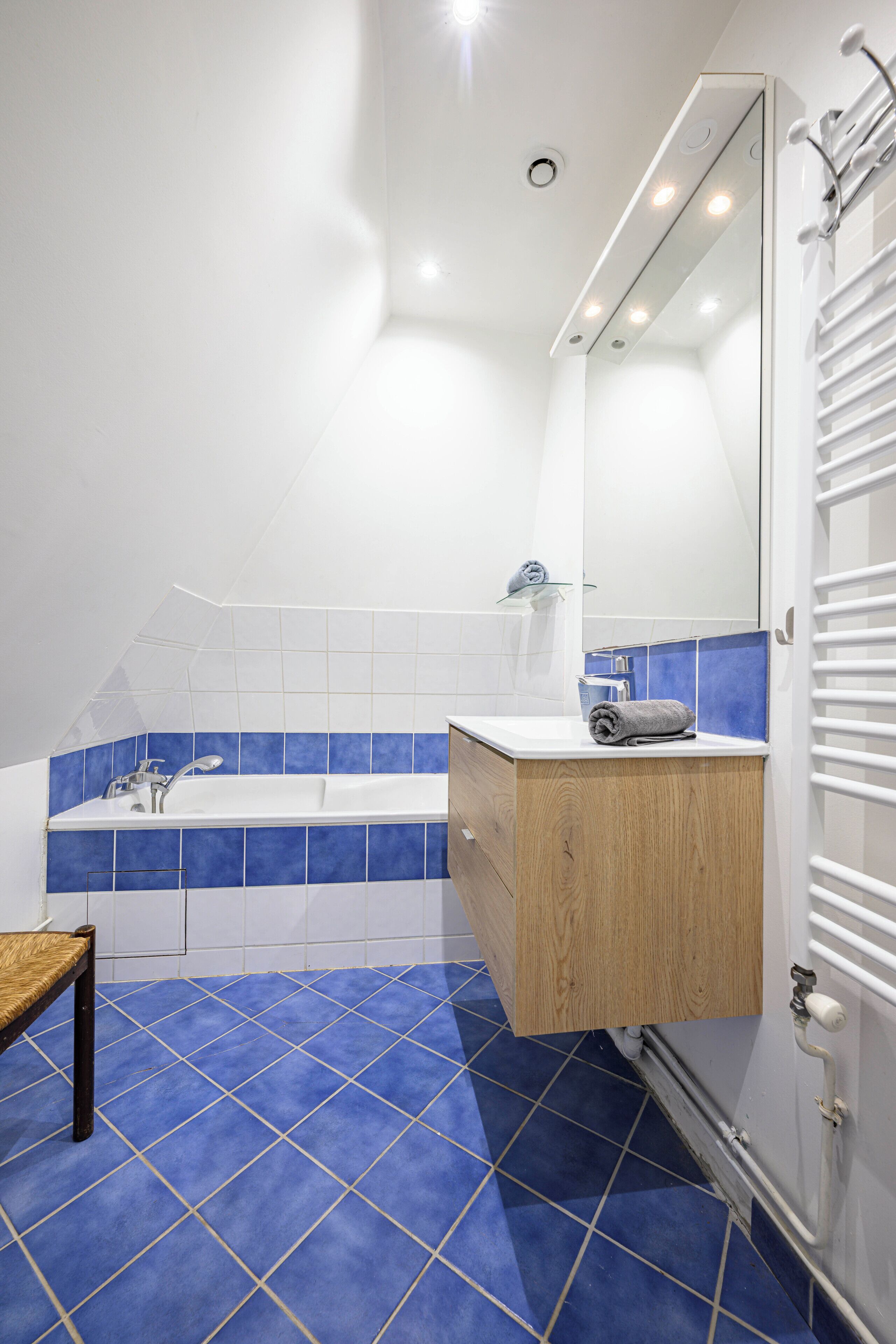 Un baño moderno con bañera, tocador de madera, espejo y suelo de azulejos azules.