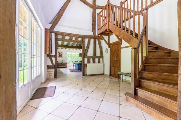 A spacious room with a wooden staircase, large windows, and a tiled floor.