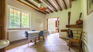A dining area with a table set for four, wooden beams on the ceiling, and a view through a window. - Beautiful cottage with heated swimming pool and large unoverlooked garden (Malleville-sur-le-Bec)