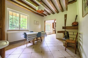 Un comedor con una mesa lista para cuatro personas, vigas de madera en el techo y vistas por una ventana.