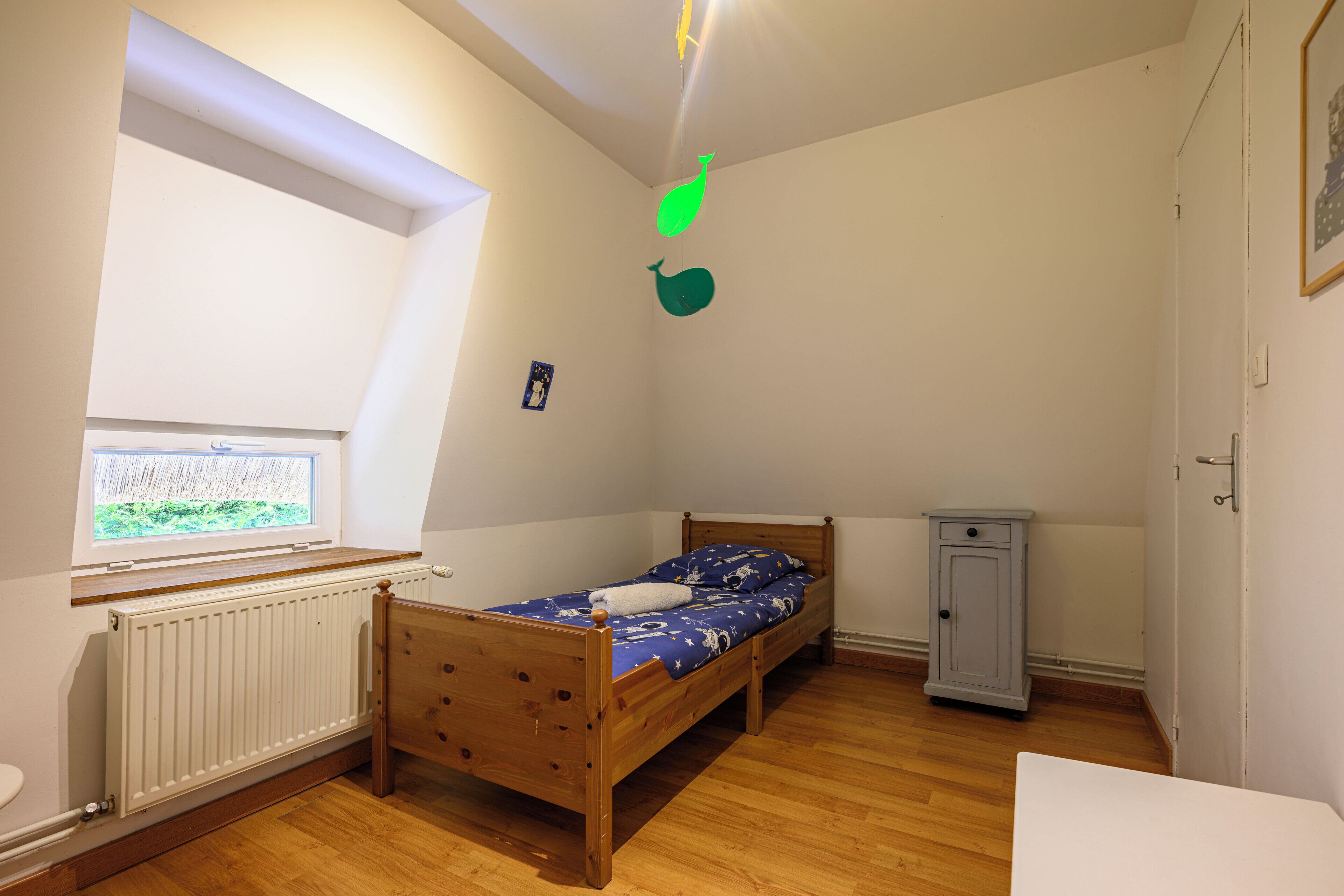 Un dormitorio con cama de madera, un archivador pequeño, una ventana y un radiador.
