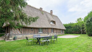 A thatched-roof house with a brick exterior, a lawn, and a table with chairs. - Beautiful cottage with heated swimming pool and large unoverlooked garden (Malleville-sur-le-Bec)
