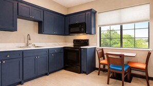 A kitchen with dark blue cabinets, a black microwave, and a window with a view of greenery. - Days Inn & Suites by Wyndham Tomball/Houston NW (Tomball)